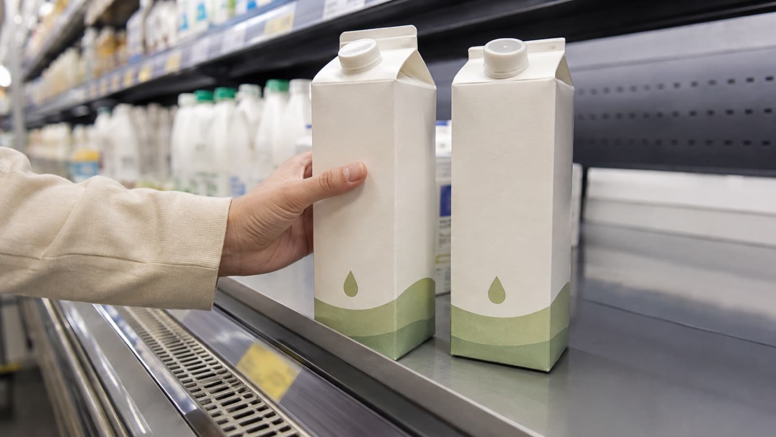 Una mano confronta due confezioni di latte davanti al banco frigo di un supermercato