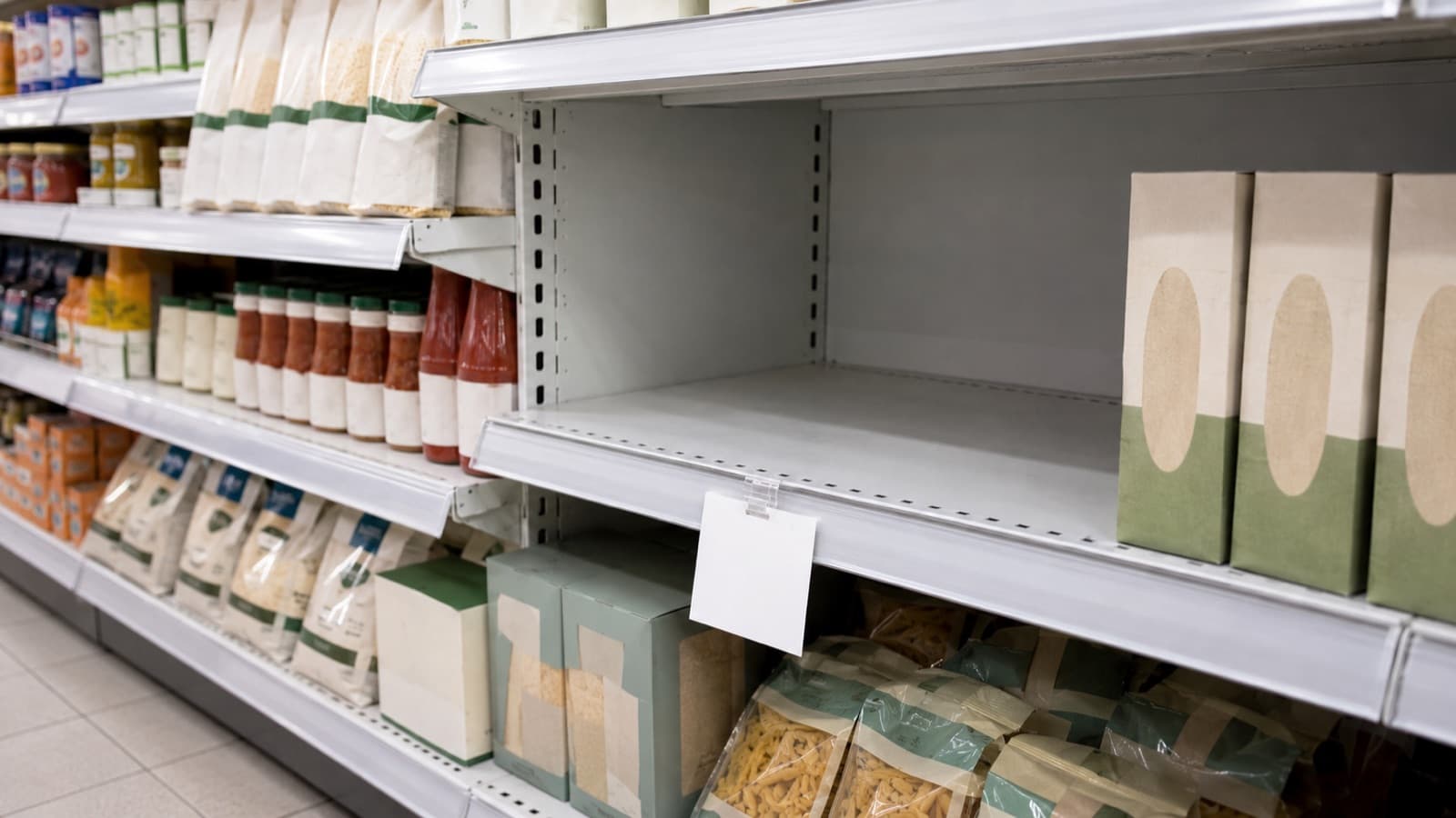 Uno scaffale di supermercato con un ripiano vuoto e un cartellino bianco appeso davanti